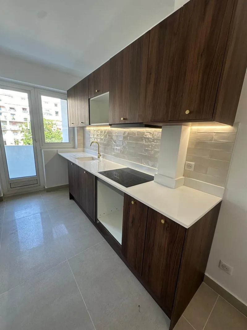 Cuisine équipée en longueur rénovée par Renovaurea : meubles bois foncé, plan de travail blanc et plaque induction
