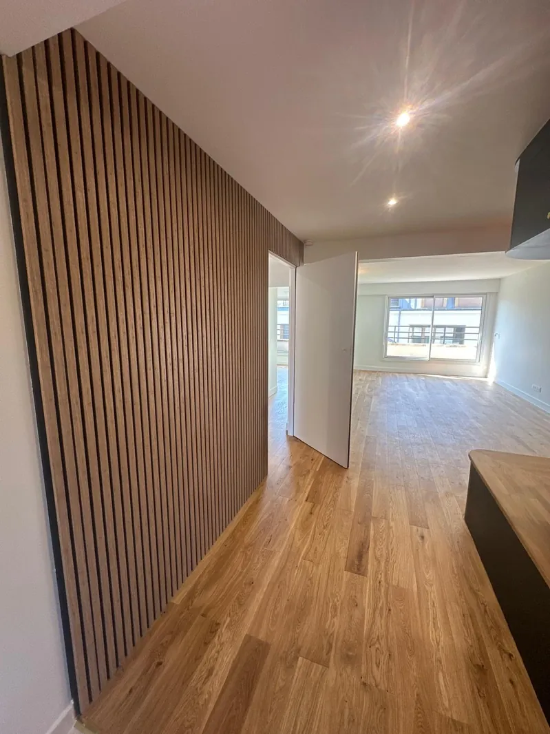 Pièce à vivre rénovée par Renovaurea avec un mur habillé de tasseaux de bois verticaux et parquet chêne