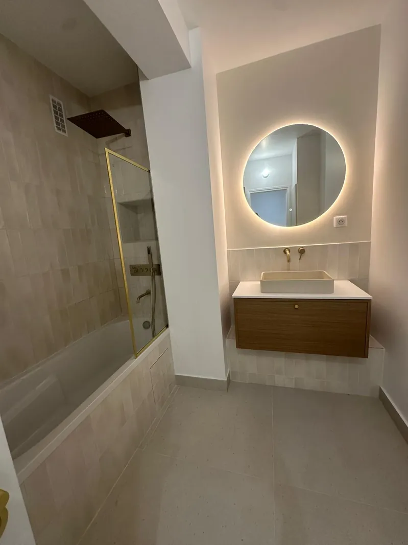 Salle de bain rénovée par Renovaurea : baignoire, colonne de douche dorée et miroir rond rétroéclairé