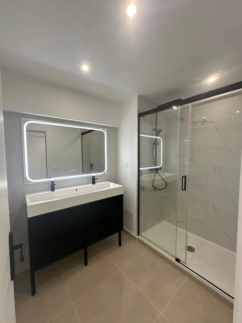 Salle de bain rénovée par Renovaurea : meuble double vasque noir, miroir rétroéclairé et douche à l'italienne