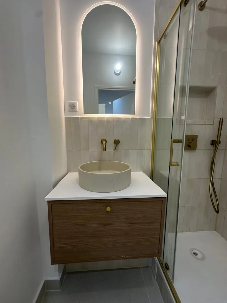 Salle d'eau rénovée par Renovaurea : vasque à poser sur meuble bois, miroir en arche et robinetterie dorée